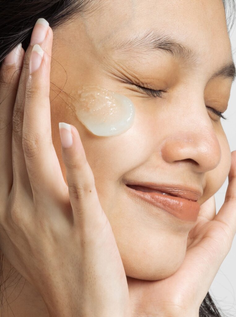 woman putting on a face serum with her eyes closed and a huge smile on her face