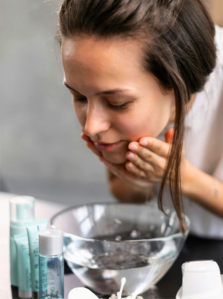 woman washing face with water in a glass bowl