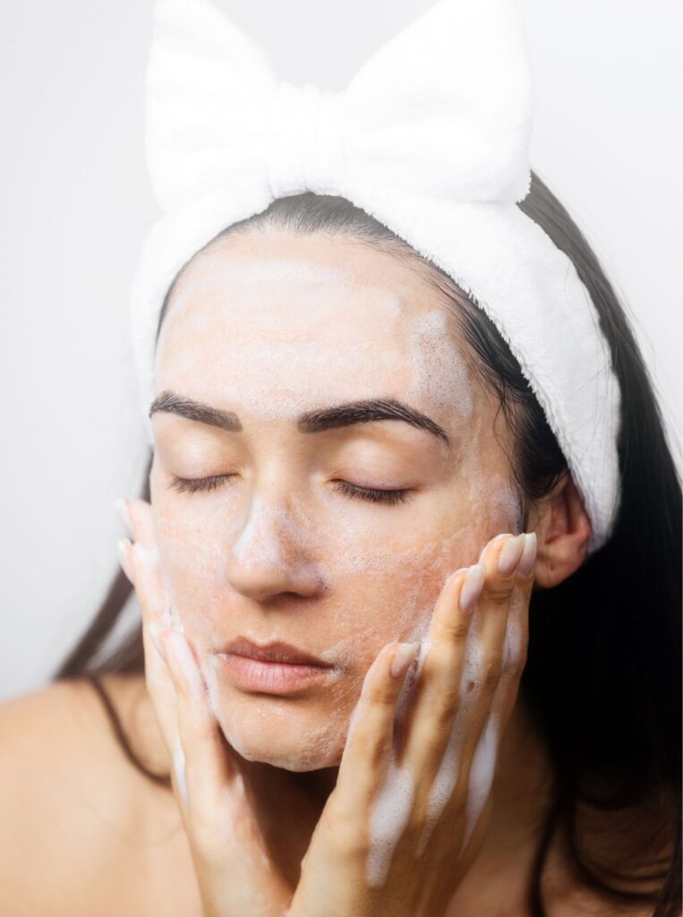 woman wearing white headband washing face with eyes closed