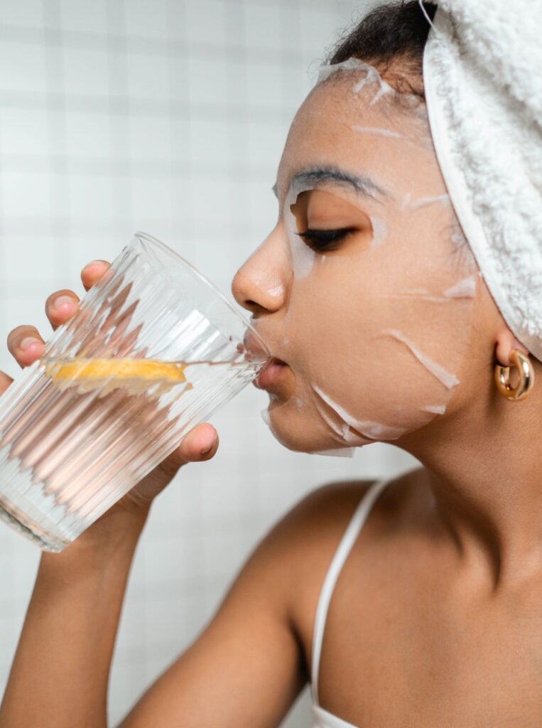 woman wearing sheet mask drinking water with lemon in it