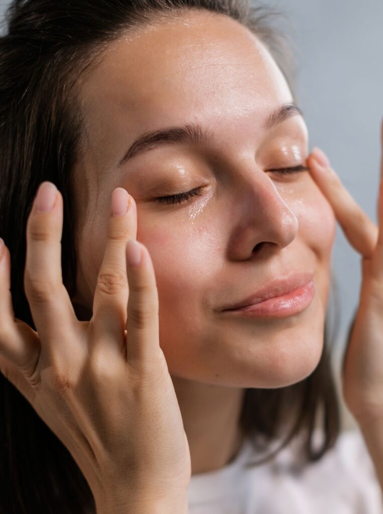 woman applying eye gel with both hands with her eyes closed and smiling