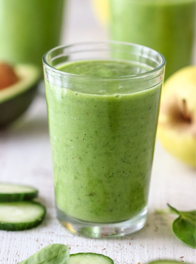 green smoothie in a glass with cucumber slices scattered around