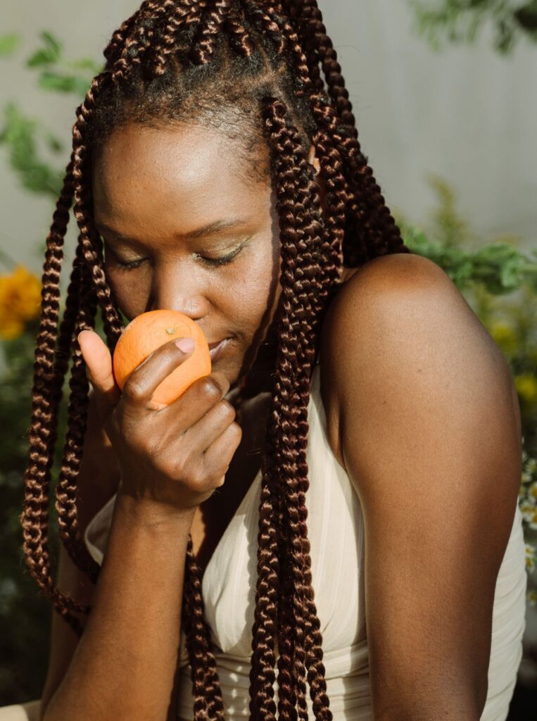 woman with braided hair sniffing an orange