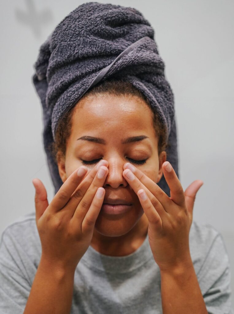 woman applying something on face with eyes closed and towel wrapped on head