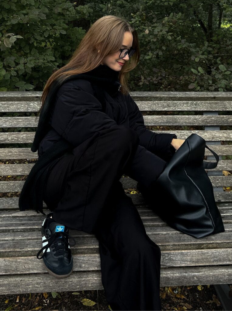 woman in all black, sitting on a bench, taking something out of a black tote bag